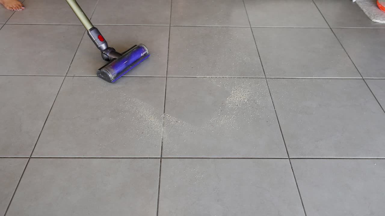 A vacuum cleaner removes crumbs from kitchen tiles, showcasing effective cleaning in a well-lit home environment