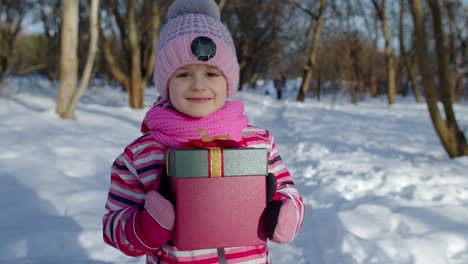 Fröhliches-Lächelndes-Mädchen-Blickt-Mit-Weihnachtsgeschenk-Geschenkbox-In-Die-Kamera-Im-Verschneiten-Winterpark