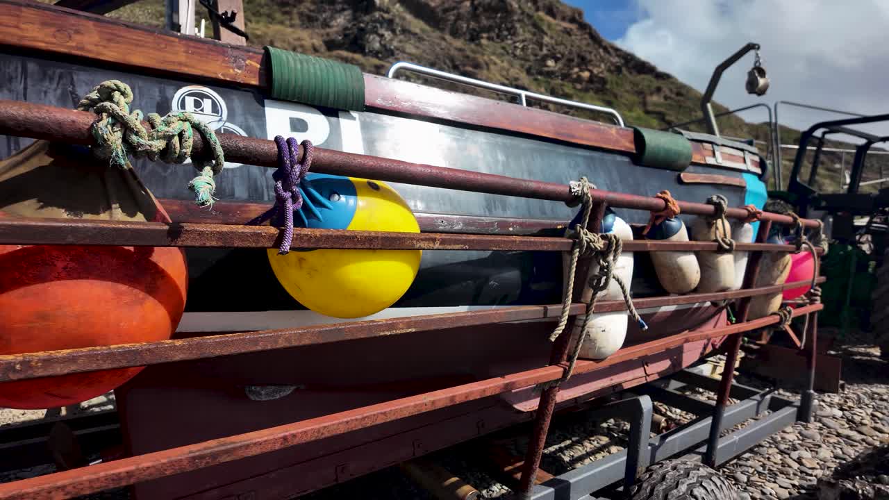 Weathered fishing boat secured on a trailer, colorful buoys and ropes tied along the rail
