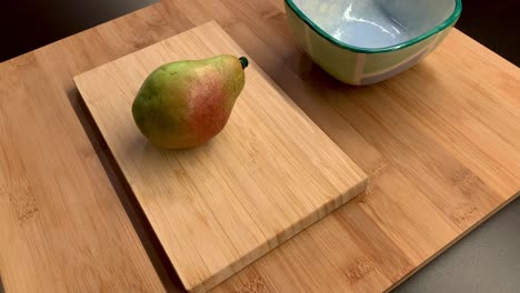 a hand placing a pear on a cutting board