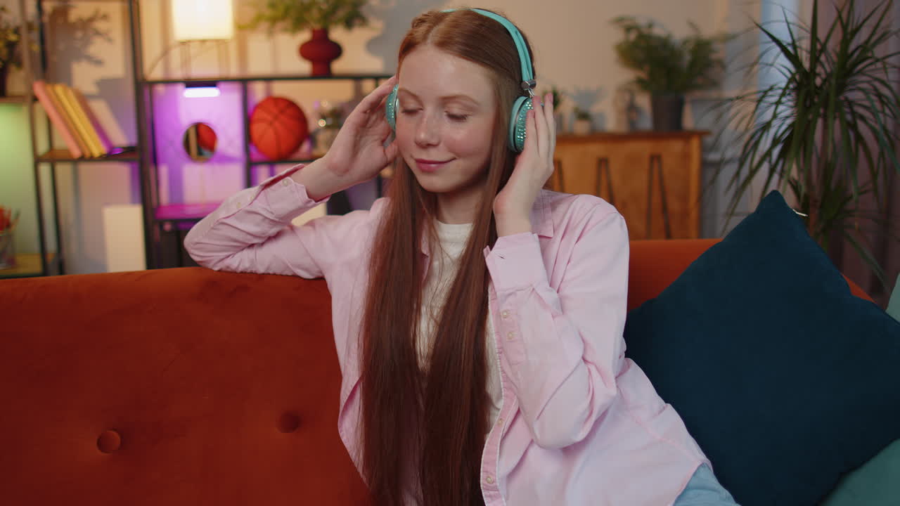 무선 헤드폰을 착용한 행복하고 편안한 아이가 집 소파에서 좋아하는 록 앤 롤 음악을 듣고 춤을 추고 있습니다.