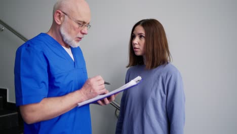 un hombre confiado con gafas un médico en uniforme azul se comunica con una joven morena y le habla de sus consejos y prevención en una clínica moderna