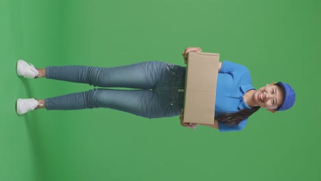 full body of asian female courier in blue uniform smiling while delivering a carton on green screen background in the studio