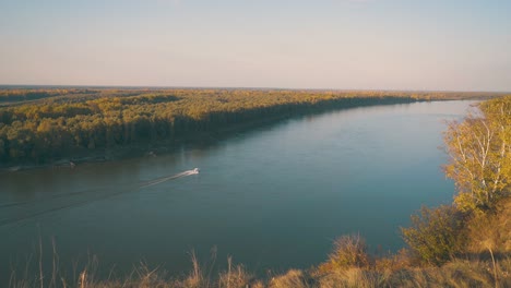 motorboat sails along calm river at dense forest in autumn