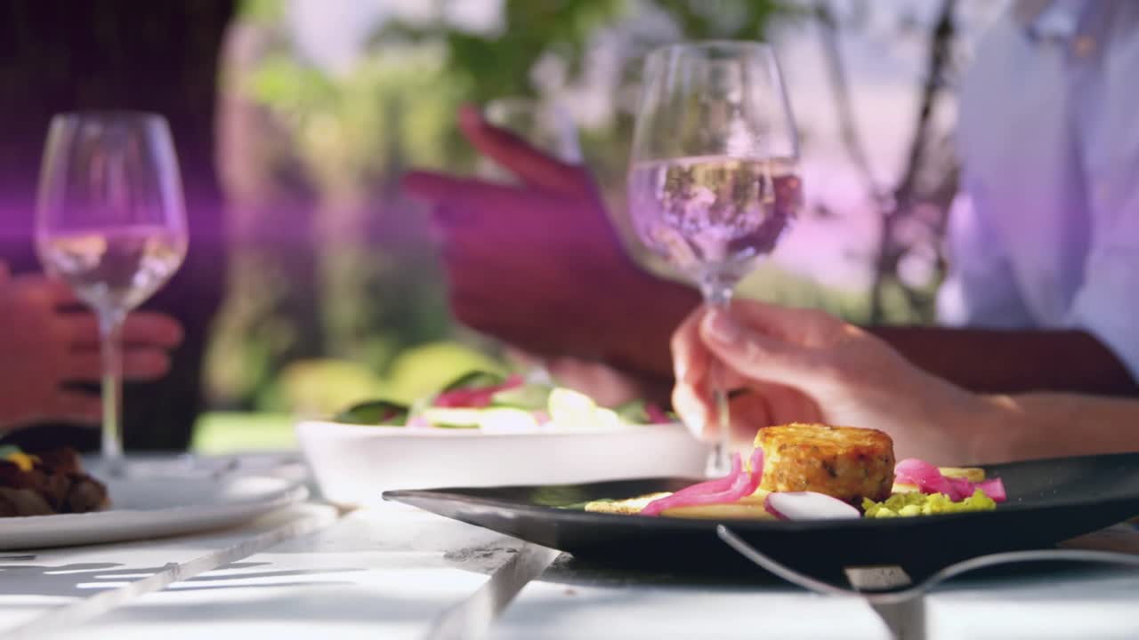 Three diners sharing dinner, hand showing item, picking salad while magenta flare obscuring hands