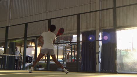 woman playing padel swings and hits the ball over the net