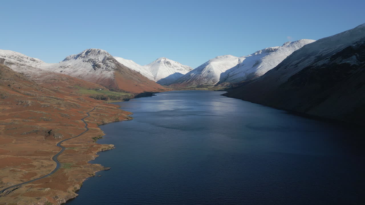 Flyvende højt over mørk sø omgivet af sneklædte bjerge ved Wasdale, Lake District, Storbritannien