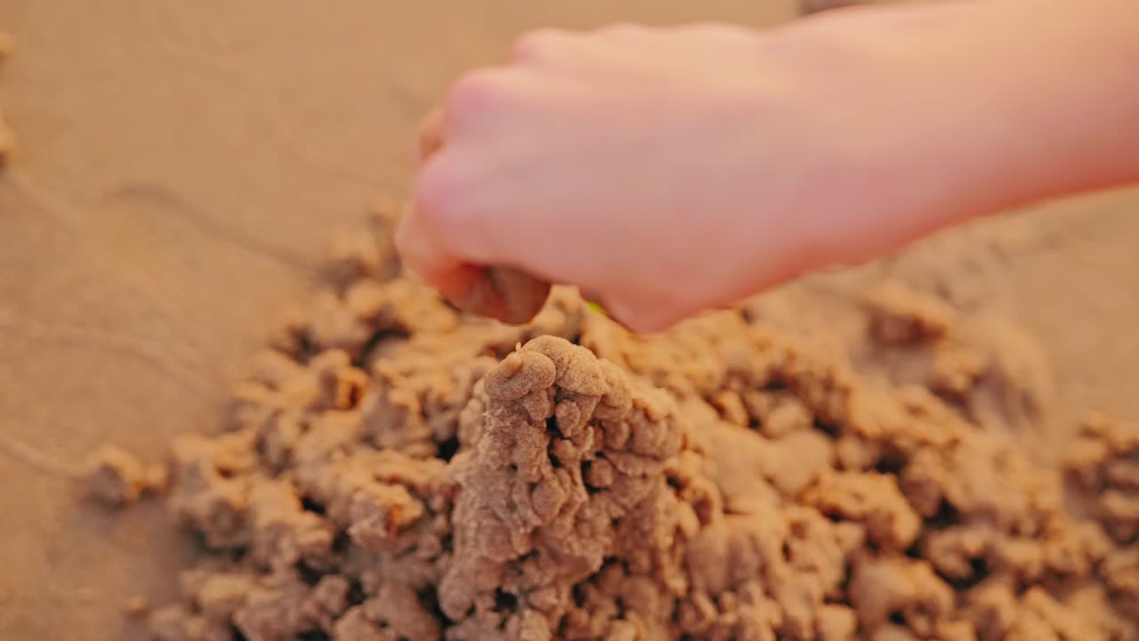 Closeup of woman’s hand forming castle shape in warm Baltic sand at sundown
