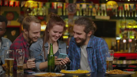 Lustige-Gesellschaft-Schaut-Sich-In-Einer-Sportbar-Ein-Foto-Auf-Dem-Telefon-An