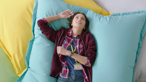 top-view-happy-caucasian-woman-student-jumping-on-colorful-pillows-smiling-relaxing-female-resting-enjoying-lunch-break-in-trendy-office-workplace