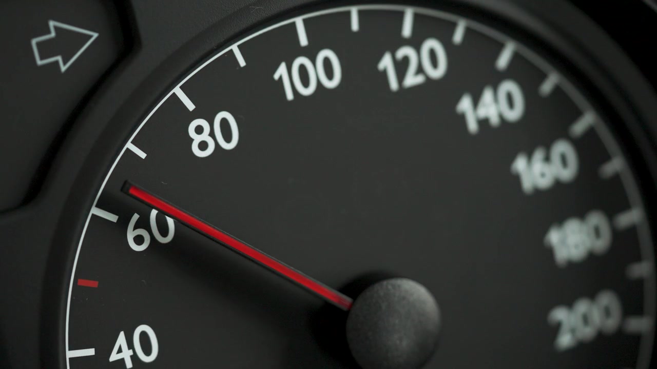 Close-up of a car speedometer showing approximately 60 kmh with a red needle and blurred blue police lights in the background. Concept image for speed control, traffic enforcement, road safety, polic