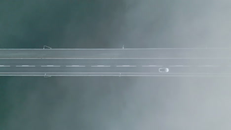 top down aerial of tesla white car driving on bridge, thick fog below, static