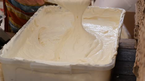 a hand mixes a white cream in a large plastic bowl