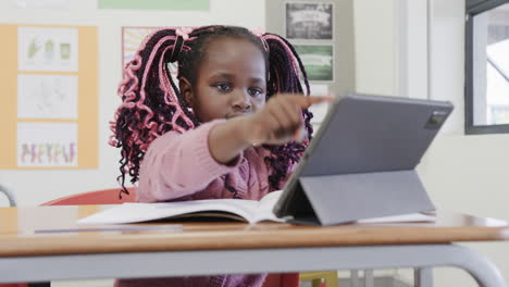 in classroom, african american girl studying with tablet and book, looking focused, at school