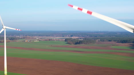 industrial wind turbines or mills in farmland of poland - aerial panoramic panning with a closeup of spinning rotor blades