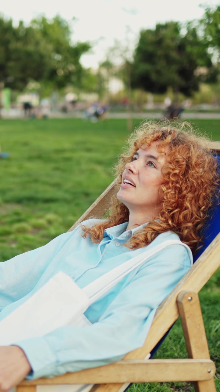 Giovane donna felice con capelli rossi ricci che si rilassa in un parco.