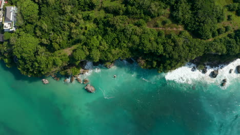 Overhead-Luftbild-Von-Tropischen-Wellen,-Die-In-Felsige-Klippen-An-Der-Küste-Von-Bali-Stürzen.-Meereswellen,-Die-In-Klippen-Mit-üppiger-Grüner-Tropischer-Vegetation-Stürzen