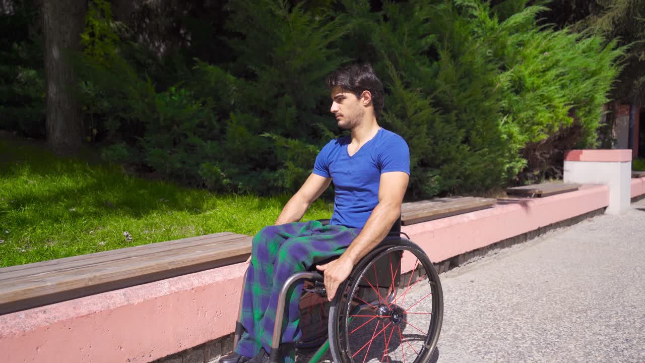⁇ 체어를 타고 있는 젊은 장애인 남자가 공원의 벤치에 앉아 있습니다.