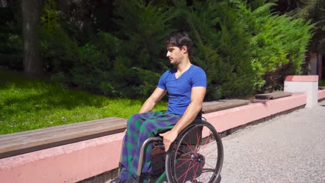 Young-disabled-man-in-a-wheelchair-sits-on-a-bench-in-the-park.