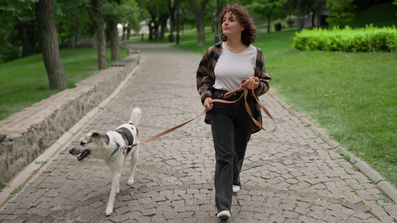 una chica morena feliz con el cabello rizado camina con su perro blanco en el parque. camina con tu mascota durante el día