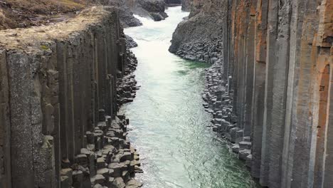 aerial shot of a turbulent river cutting through a dramatic basalt column canyon in the stark icelandic landscape