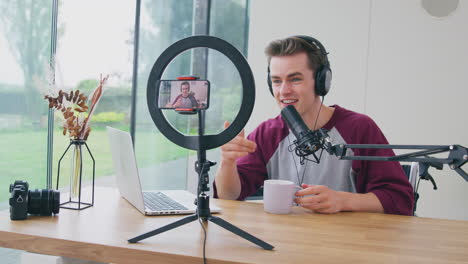 vlogger masculino con auriculares con micrófono transmitiendo en vivo en el teléfono móvil