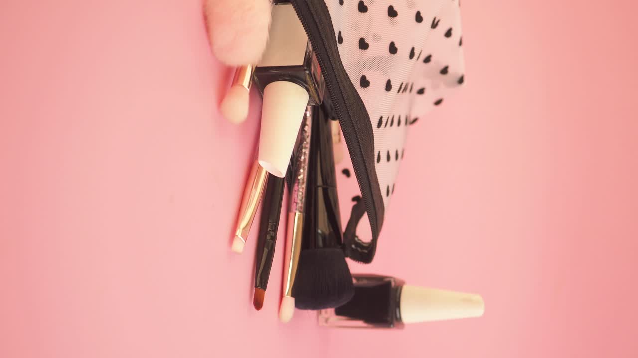 Makeup Brushes and Cosmetics Spilling from a Bag on a Pink Background