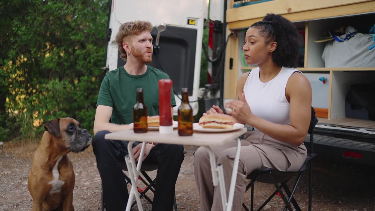 Couple eating outdoors with dog near van