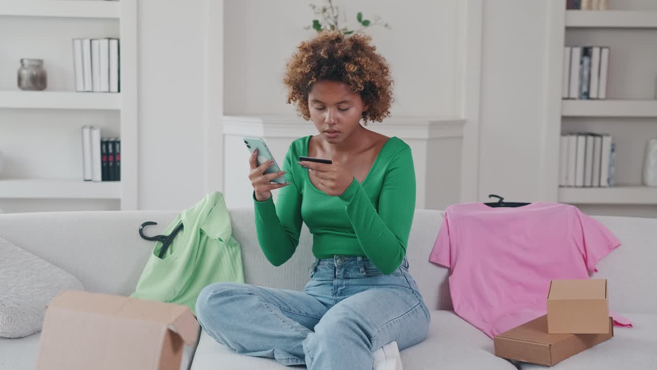 joven afroamericana con teléfono móvil y tarjeta de crédito se sienta en el sofá