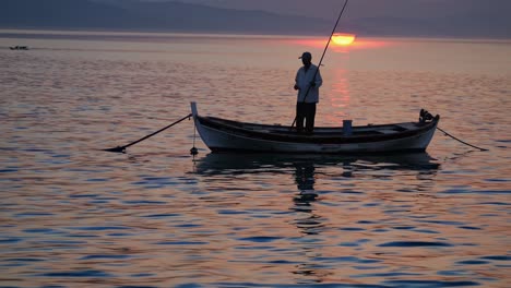 silhouette of a fisherman standing on his small boat and fishing during a beautiful sunset over the calm sea, creating a peaceful and serene atmosphere