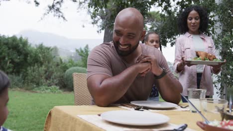 Happy-biracial-parents,-son-and-daughter-serving-meal-at-dinner-table-in-garden,-slow-motion