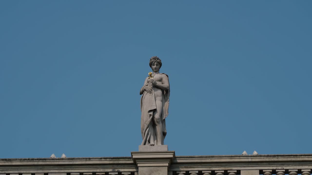 Stone statue with crown holds a golden rose atop Prague’s National Museum facade