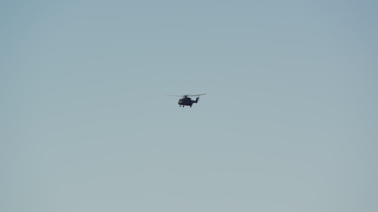 Mørk helikopter flyver langsomt over en klar blå himmel