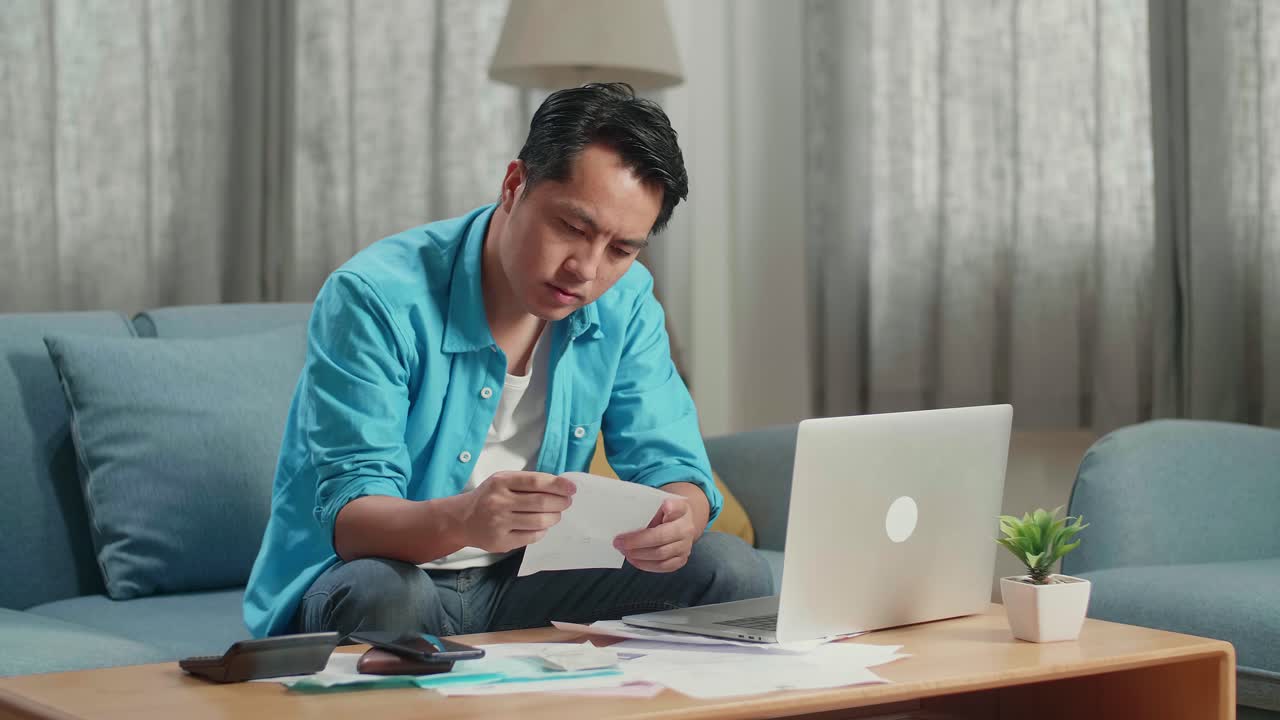 Pria Asia Melihat Tagihan dan Berpikir Sambil Bekerja dengan Laptop di Rumah