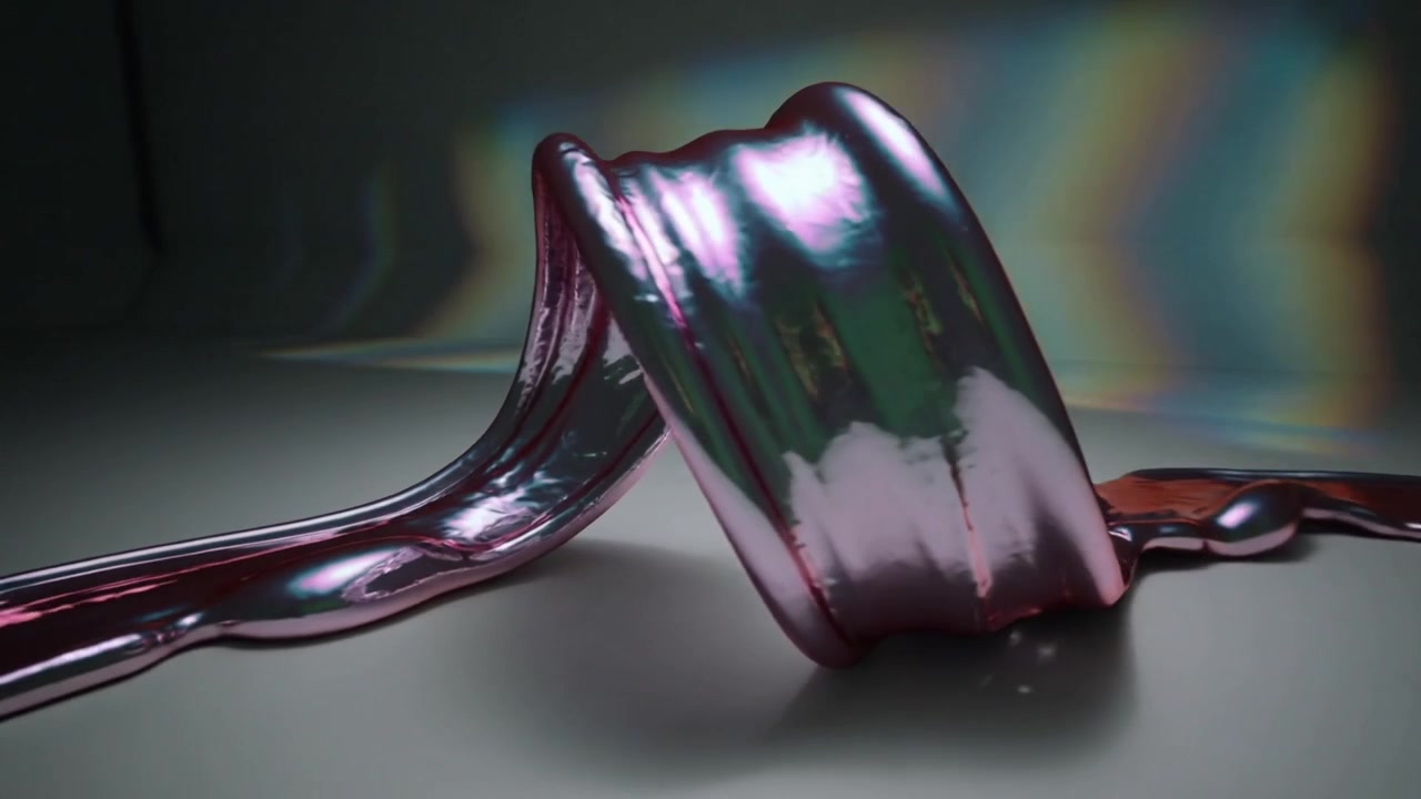 Curling iridescent ribbon material forming tight coil on matte tabletop, with prism rainbow