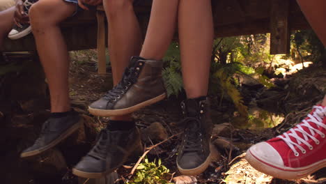 people sitting on a small bridge in forest, close up of legs