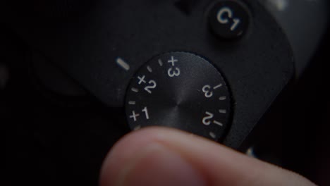 macro closeup, person's finger adjusting camera flash exposure compensation wheel