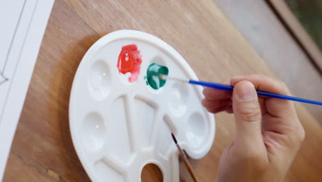 Close-up-of-hand-holding-brush-mixing-watercolor-painting