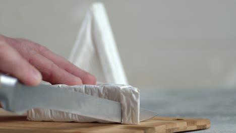 male hand with knife cut camembert cheese into small pieces.