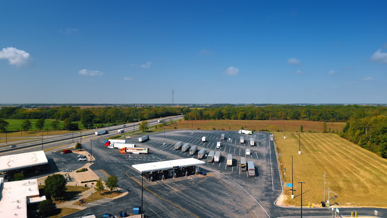 Chicago, USA, 29 June 2025: Approaching gas station and a parking lot with parked trucks. A highway and lush green forests at backdrop. Aerial view
