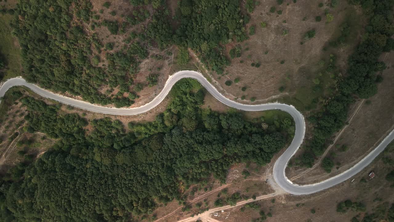 Toma aérea cenital de una carretera sinuosa que cruza un denso bosque verde en Turquía en un día nublado.