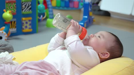 cute asian baby drinking milk from bottle and playfully moving up and down