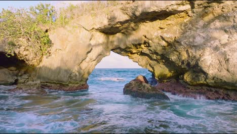 low angle drone shot of famous natural arch with crashing waves of caribbean sea - aerial forward flight