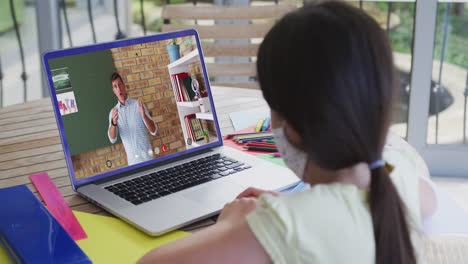 Colegiala-Caucásica-Con-Mascarilla-Usando-Una-Computadora-Portátil-En-Videollamada-Con-Un-Maestro