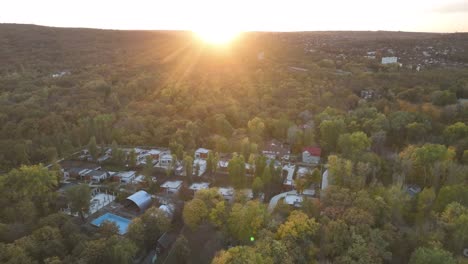 Bei-Sonnenuntergang-Diagonal-Am-Horizont-über-Einer-Stadt-Fliegen,-Die-Im-Herbst-Zwischen-Bäumen-Im-Wald-Liegt