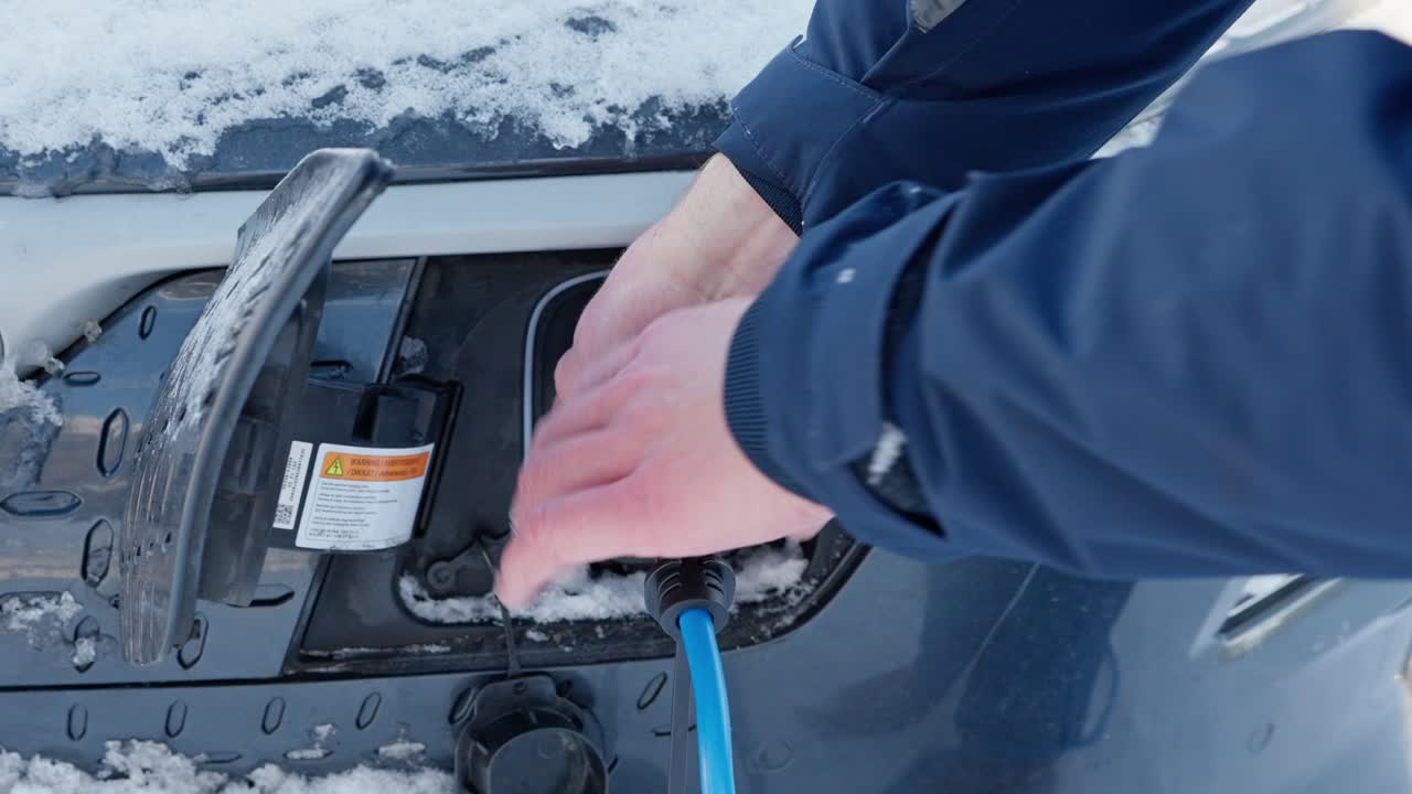 Man tries to remove frozen charging cable from electric car on Winter morning in Norway.