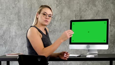 business lady talking to the camera in the office pointing to the screen on the computer. green screen mock-up display