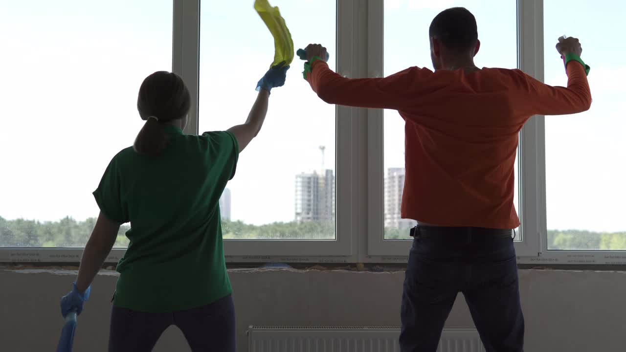 vista trasera de las siluetas de una mujer y un hombre bailando y preparándose para limpiar en un apartamento de la ciudad. trabajadores positivos de una compañía de limpieza profesional limpian las ventanas y disfrutan del baile.