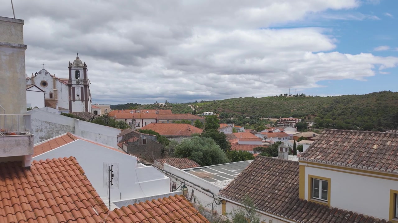 Uma vista tranquila da cidade de Silves com telhados laranja e colinas verdes exuberantes sob um céu nublado