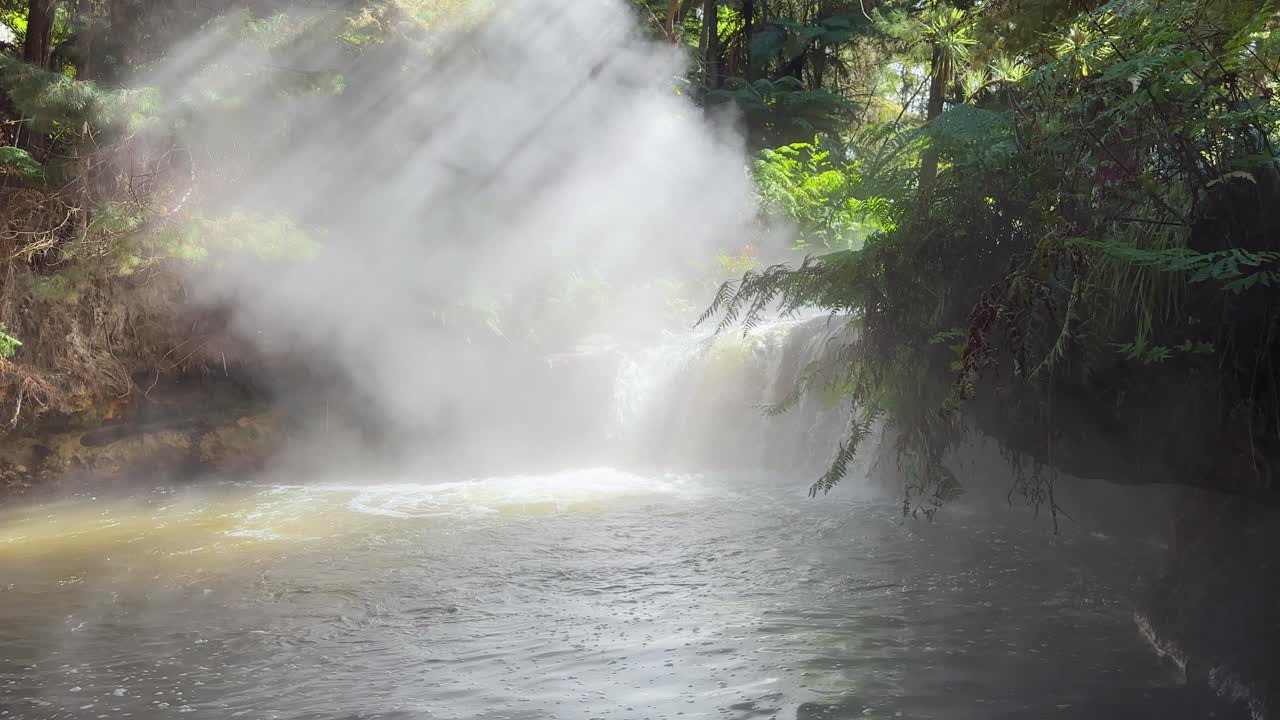Steam rises from the warm waters of Kerosene Falls, a natural hot spring in New Zealand. Surrounded by lush greenery, the scene highlights the country’s geothermal beauty